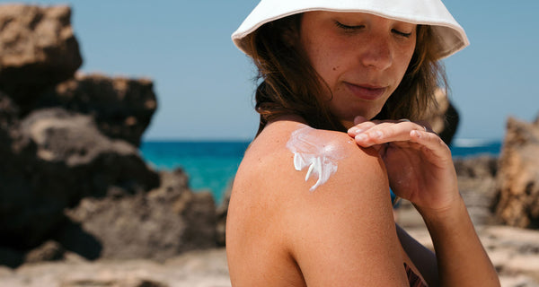 Woman at the beach applying mineral sunscreen on her shoulder | ATTITUDE